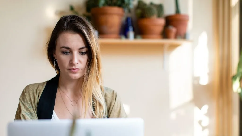 Woman working on laptop at home with sunshine and plants